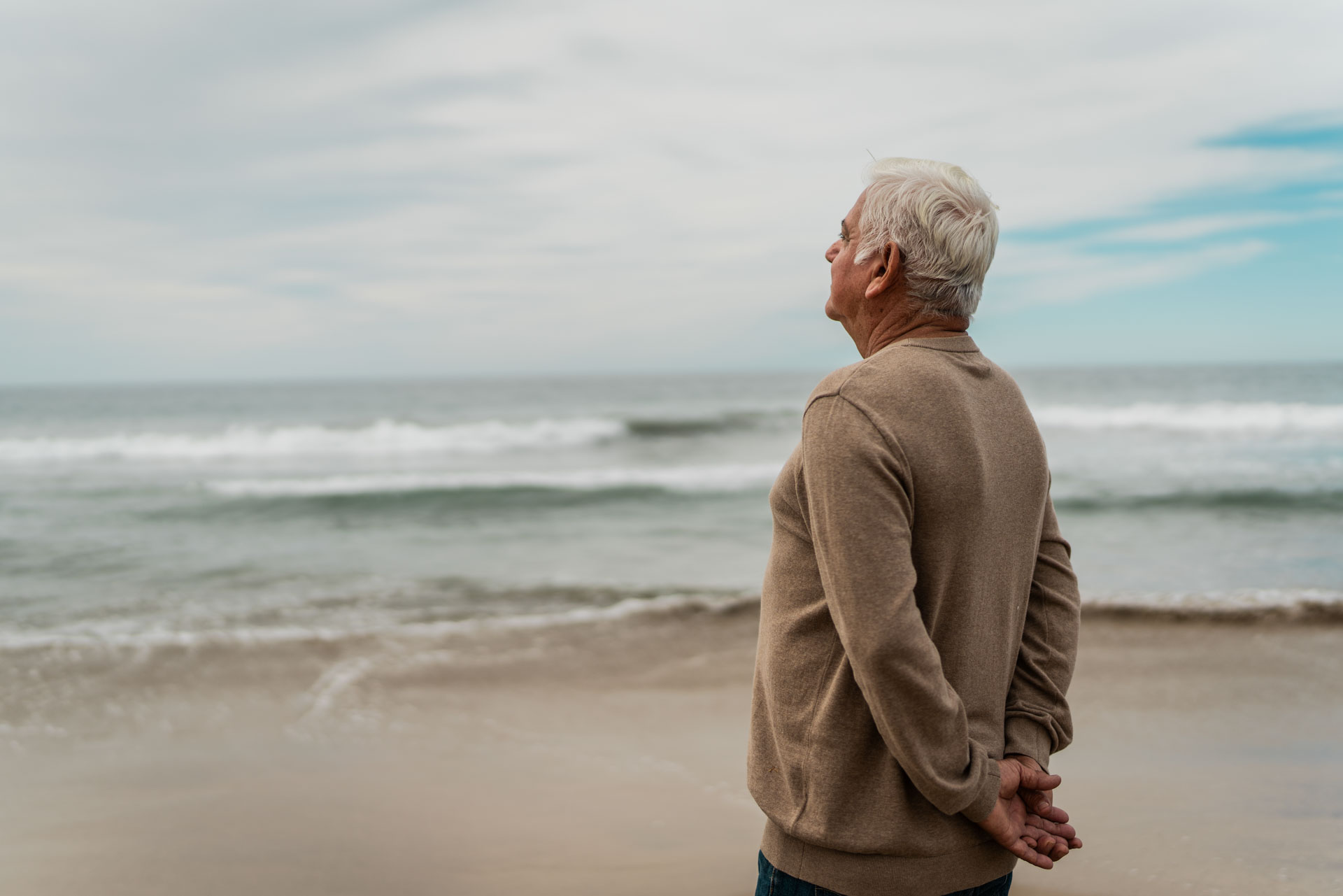 Ein älterer Mann, der nachdenklich am Strand in die Ferne blickt